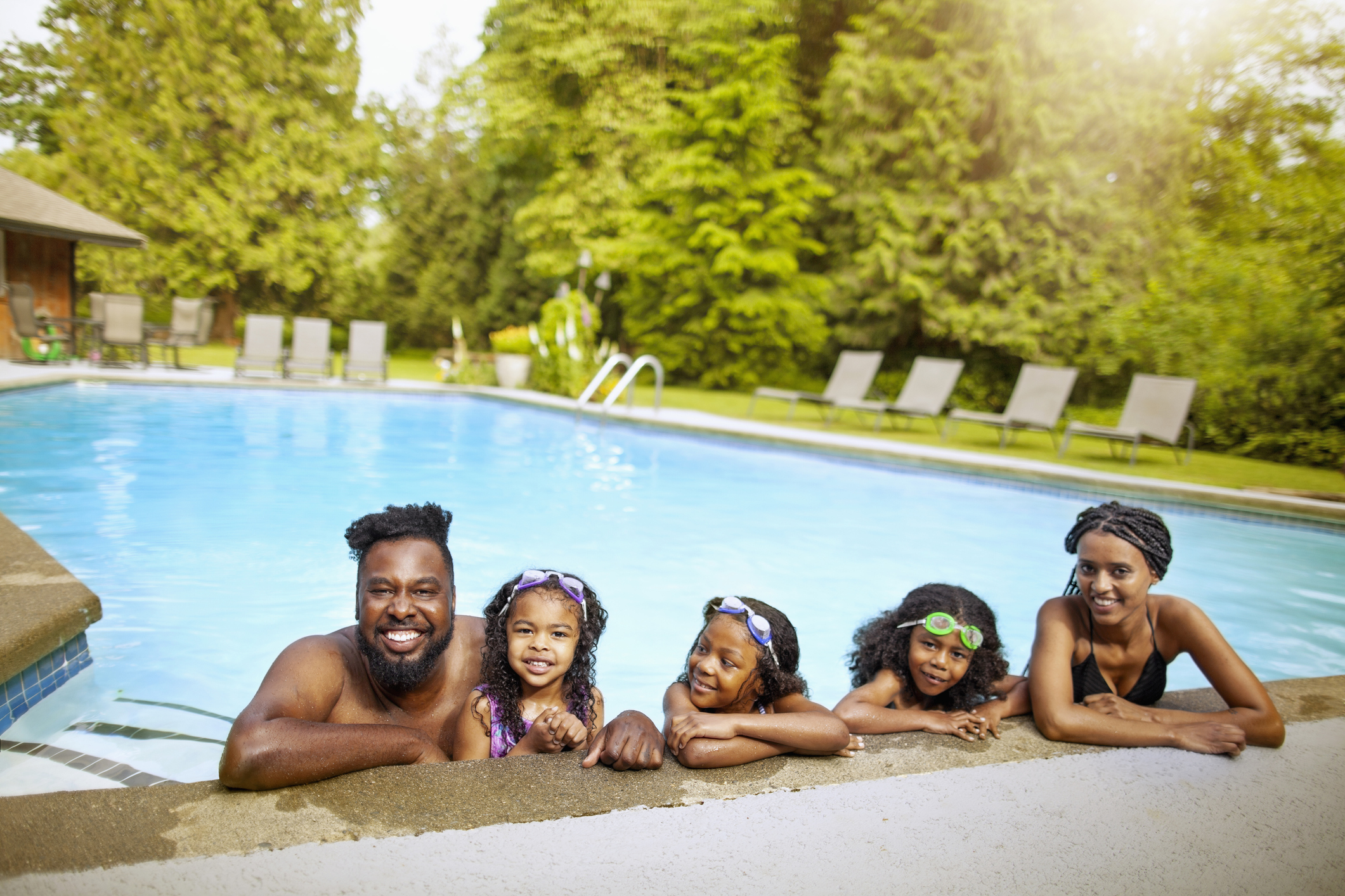 Portrait of African-American family with three children relaxing at backyard water pool